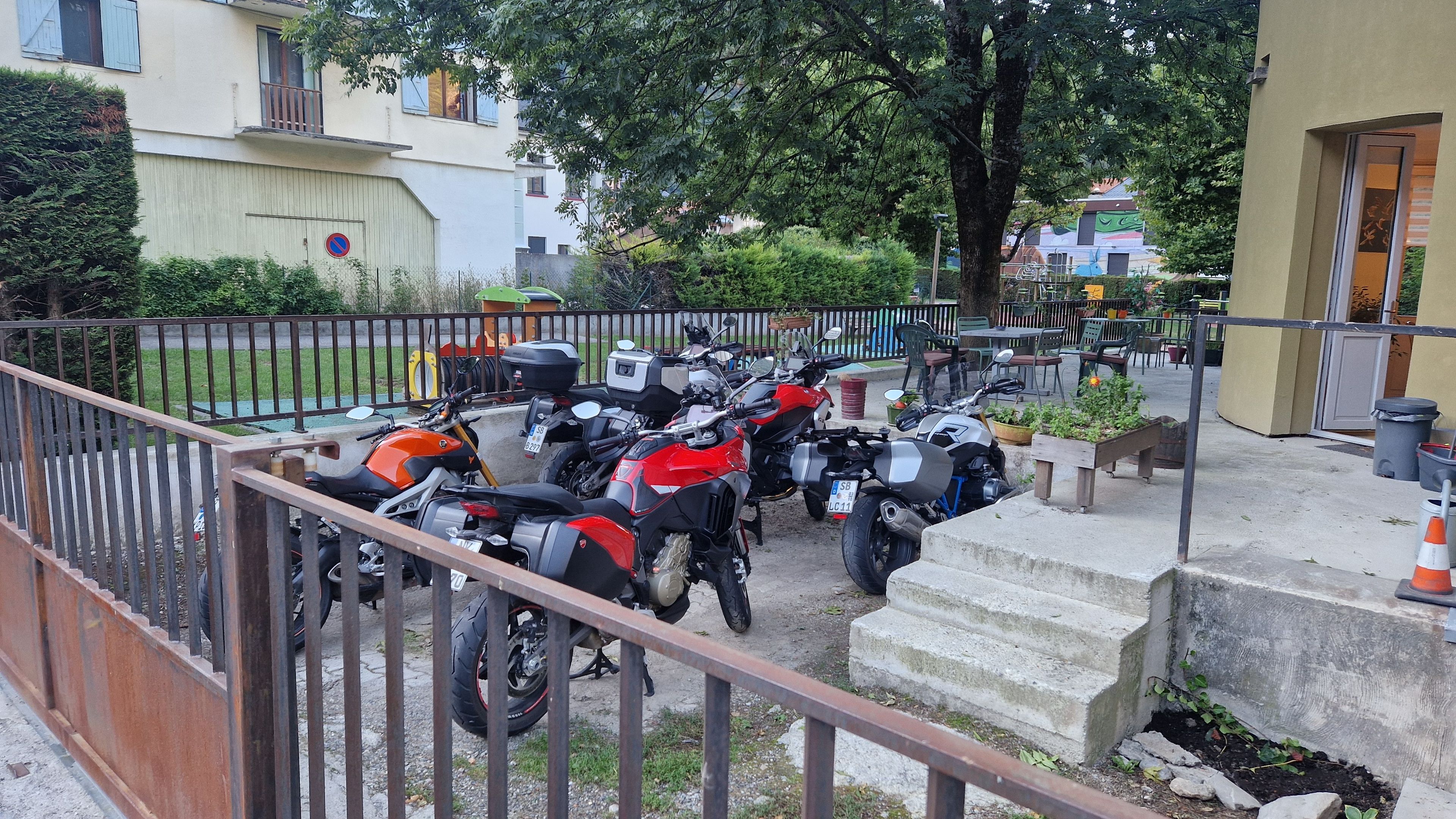 Een rij motorfietsen langs een stoeprand, met een metalen hek op de voorgrond en een gebouw met een balkon op de achtergrond.