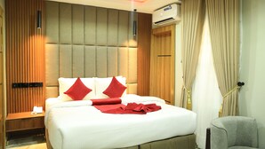 A hotel room with a large bed, a nightstand, a chair, a wooden panel wall, and an air conditioning unit. - Victoria Plus Hotel & Suites (Asaba)