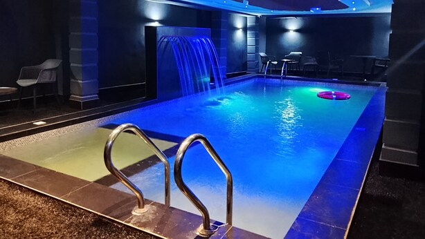 An indoor swimming pool with a waterfall feature, seating area, and a poolside bar. - Victoria Plus Hotel & Suites (Asaba)
