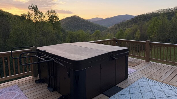Eine Terrasse mit Whirlpool, Holzgeländern und Blick auf ein bewaldetes Tal.