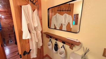 A bathroom with wooden flooring, a mirror, a toilet, and a towel rack with robes.