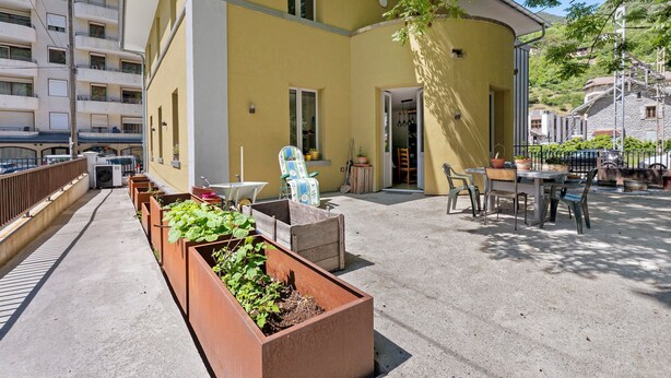 A yellow building with a balcony, outdoor seating, and a garden area with planters. - Room 5 – Le Toit Vert Inn: Space and Shared Moments in Moutiers (Moûtiers)
