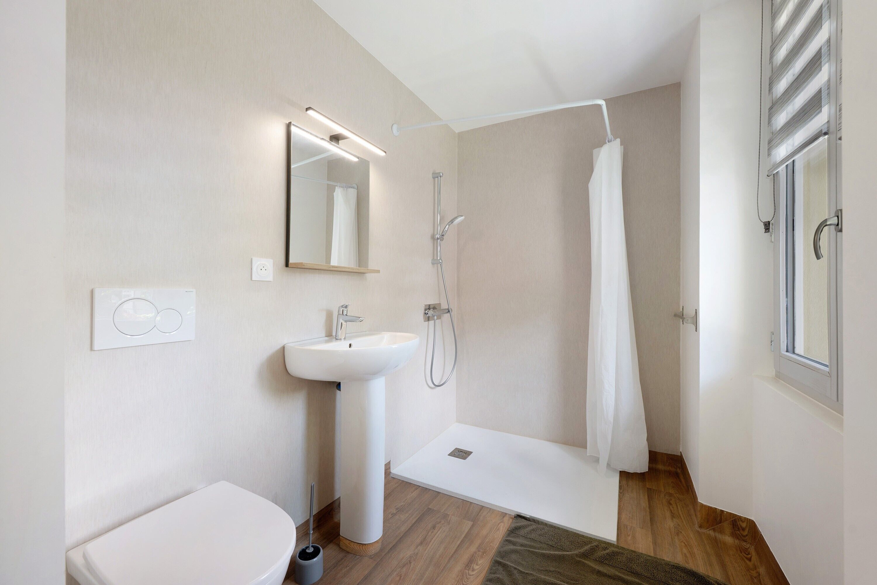Une salle de bain moderne équipée de toilettes, d’un lavabo, d’une douche et d’une fenêtre.