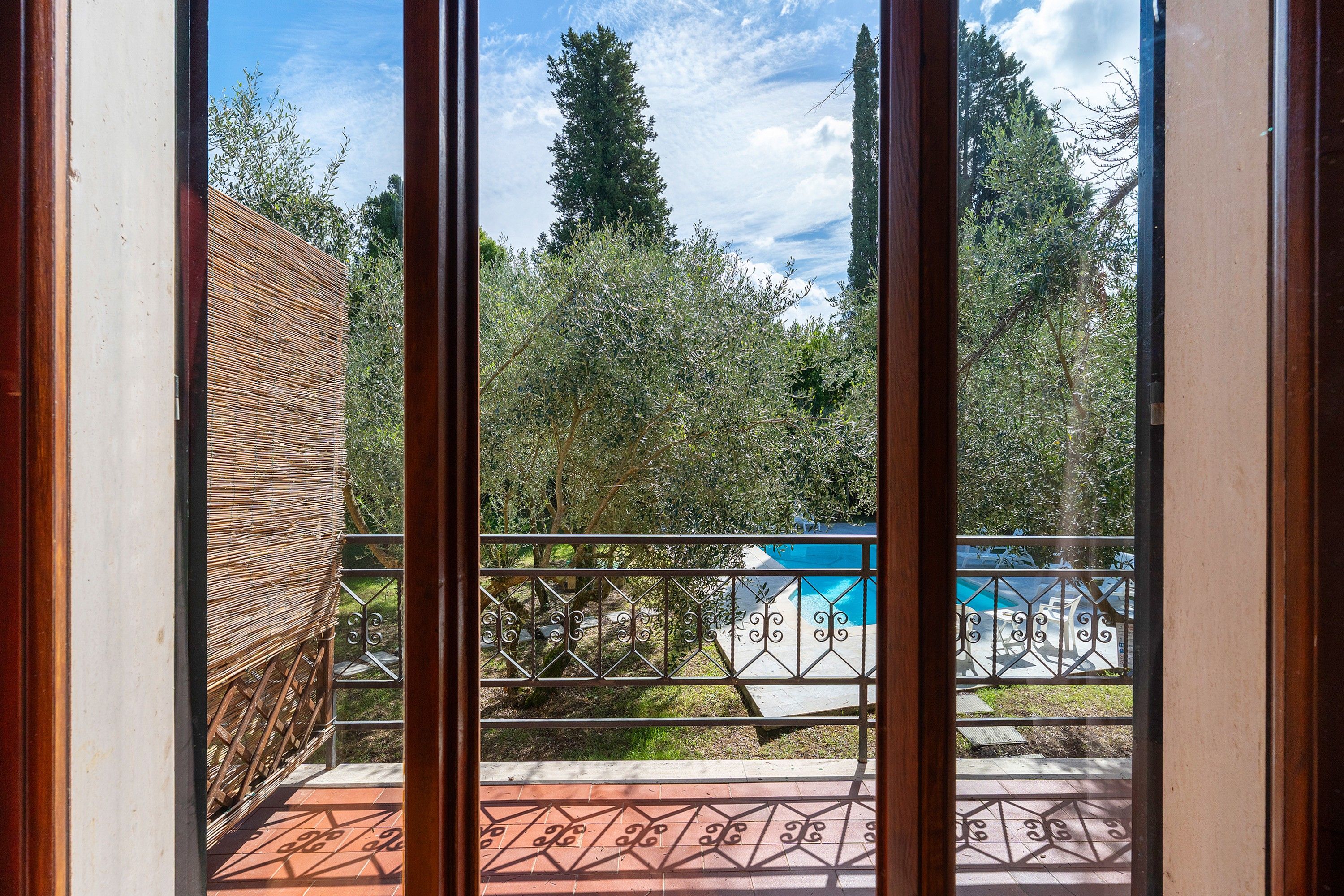 Vista a través de una ventana con barandilla de metal, un patio con baldosas y una zona de piscina con piscina azul.