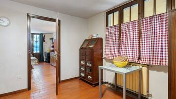 A kitchen with a wooden cabinet, a table with a yellow bowl, and a window with checkered curtains.