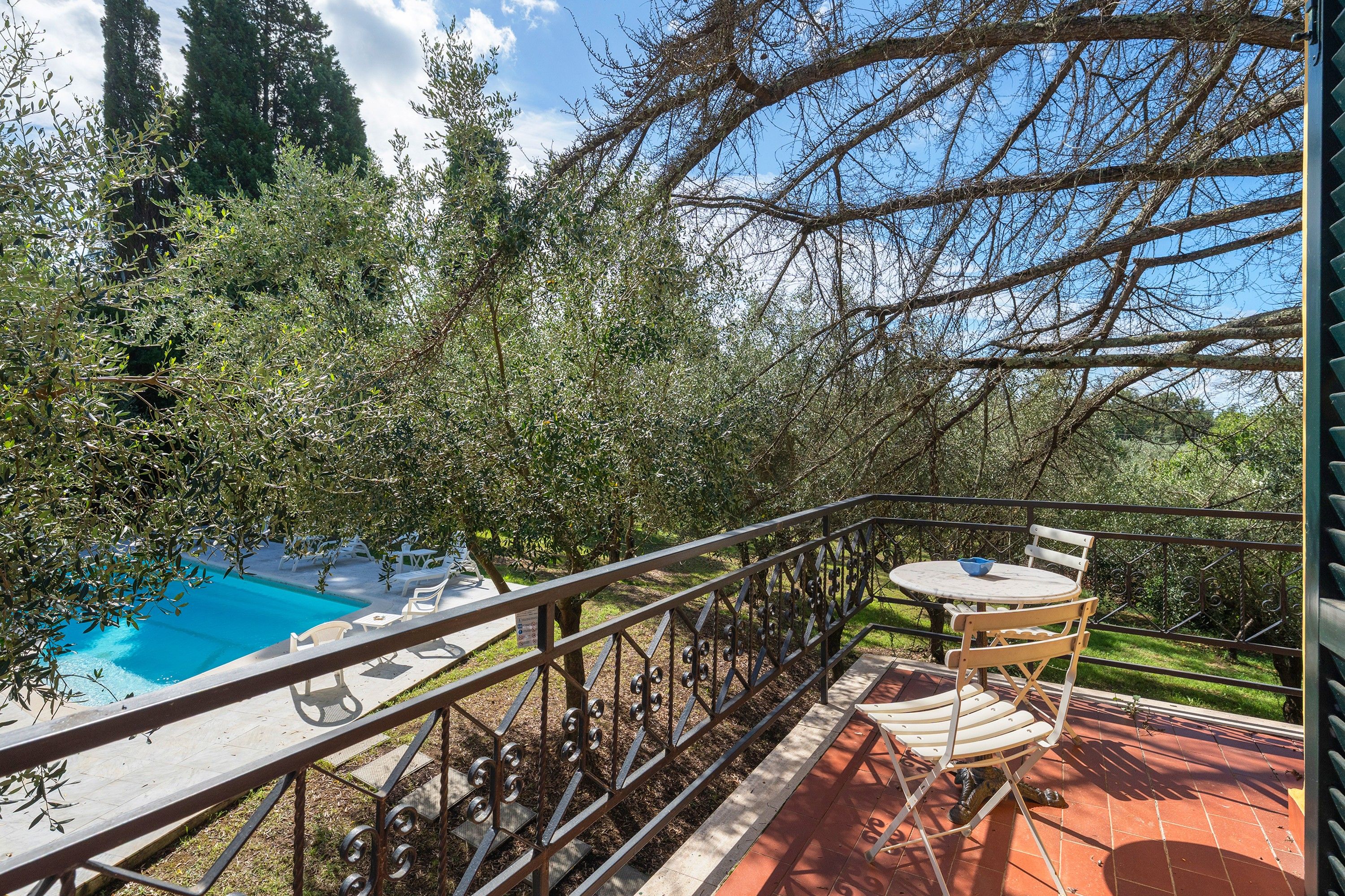 Un balcón con piscina, mobiliario exterior y vistas a árboles y al cielo.