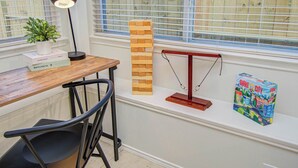 Ein Holztisch mit Lampe, Pflanze und Büchern, ein Turm aus Holzklötzen, eine Waage und eine Spielesammlung auf einem Fensterbrett.