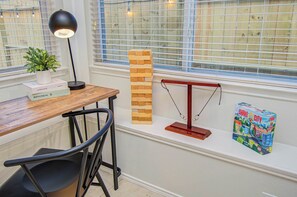 Ein Holztisch mit Lampe, Pflanze und Büchern, ein Turm aus Holzklötzen, eine Waage und eine Spielesammlung auf einem Fensterbrett.