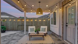Eine Terrasse im Freien mit Holzlattenzaun, zwei weißen Polsterstühlen, einem Holztisch und Lichterketten.