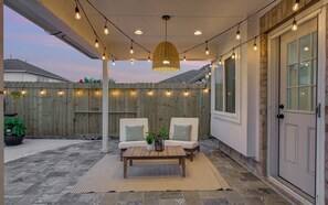 Eine Terrasse im Freien mit Holzlattenzaun, zwei weißen Polsterstühlen, einem Holztisch und Lichterketten.