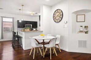 A modern kitchen with dark cabinets, a white island, and a round dining table with white chairs. - 3/2 Cozy Home Near UNT & Twu-pool, Bbq, Gym, Games (Denton)