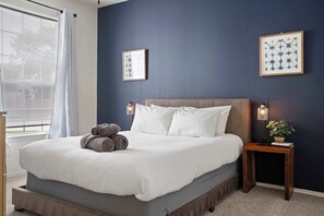 A bedroom with a bed, two wall-mounted lamps, a nightstand with a plant, and a window with blinds. - 3/2 Cozy Home Near UNT & Twu-pool, Bbq, Gym, Games (Denton)