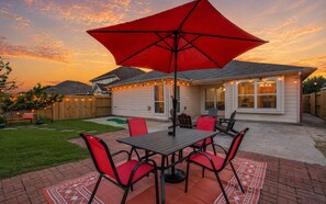 Eine Terrasse mit Tisch, Stühlen, einem roten Sonnenschirm und Lichterketten.