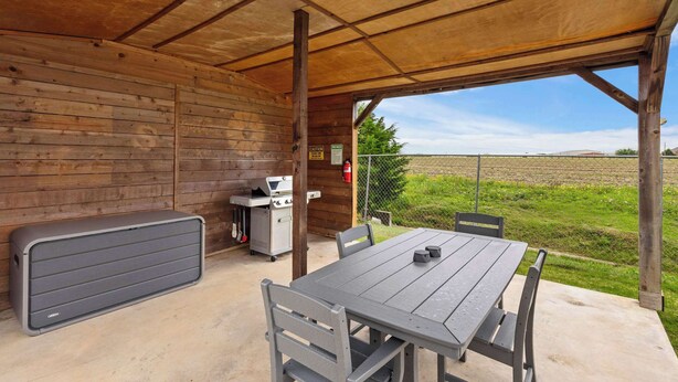 An outdoor covered patio with a table and chairs, a barbecue grill, and a storage bench. - Heart of Ferris: 3-bd/2-ba With Pool, Patio & BBQ (Ferris)