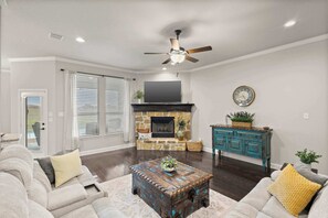 A living room with a stone fireplace, a ceiling fan, a television, and a blue cabinet. - Heart of Ferris: 3-bd/2-ba With Pool, Patio & BBQ (Ferris)