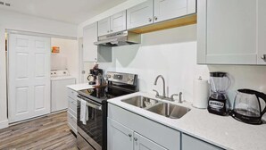 A modern kitchen with white cabinets, a stainless steel sink, a stove, and a coffee maker. - Serene Escape - Peaceful 3-bd Retreat With Yard (Grand Prairie)