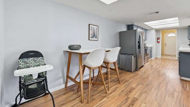Cozinha moderna com área de jantar, teto alto com claraboias e porta visível para outro cômodo.
