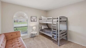 Um quarto com uma cama beliche, uma mesinha com abajur e uma janela com persianas.