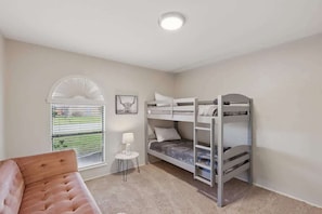 Ein Schlafzimmer mit Etagenbetten, einem kleinen Tisch mit Lampe, einem Fenster mit Jalousien und Blick ins Freie.