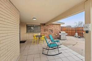 Eine Terrasse mit gelben Stühlen, einem blauen Schaukelstuhl und einem Grill.
