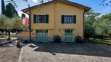 A two-story building with a yellow facade, green shutters, and a stone-paved entrance.