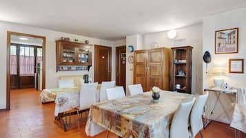 A dining area with a table set for four, surrounded by white chairs. There is a wooden cabinet with glass doors containing kitchenware.