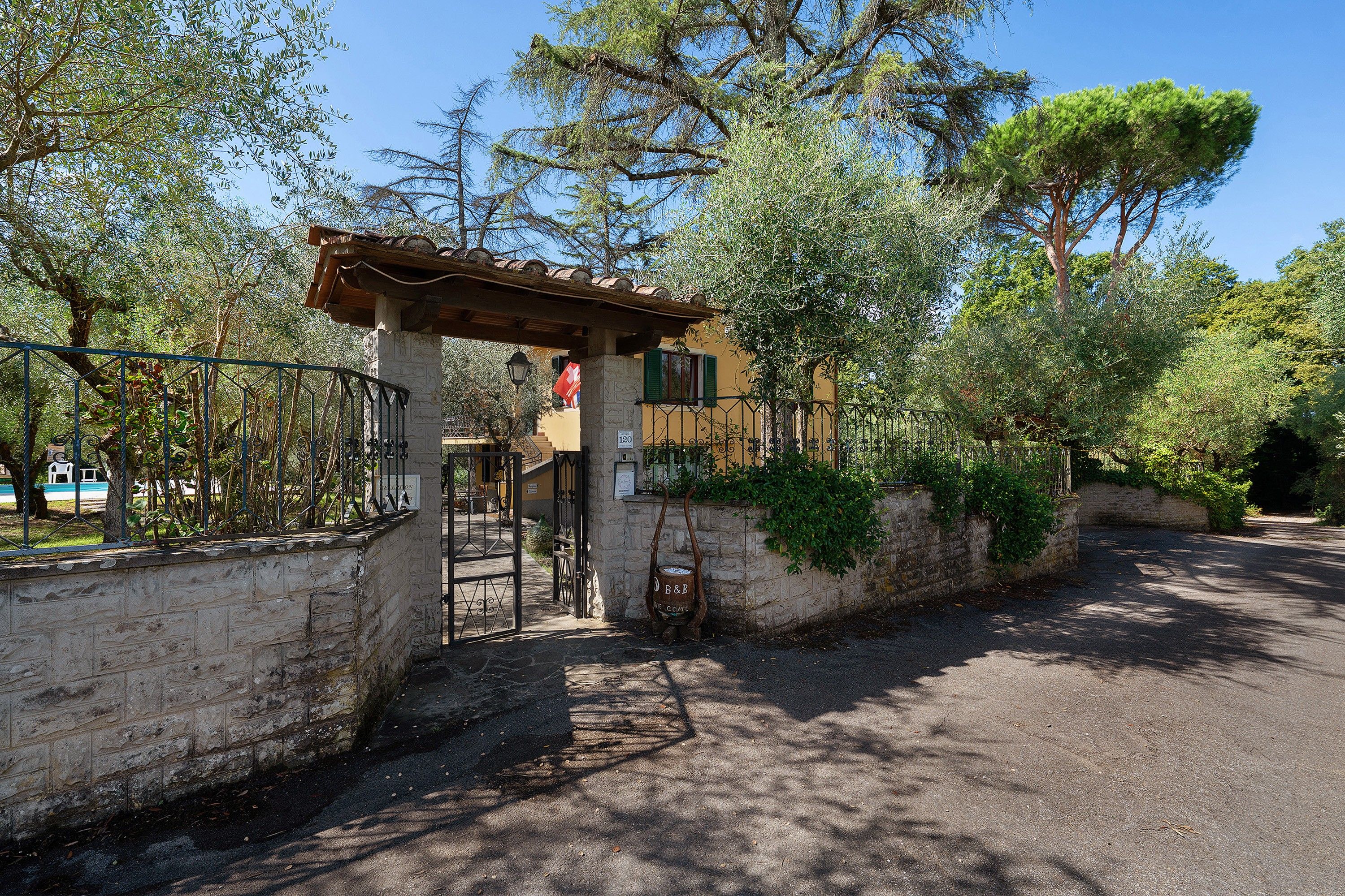 A gated entrance with a stone wall, a metal gate, and a pergola structure.