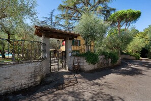 Una entrada protegida con un muro de piedra, una reja metálica y una estructura de pérgola.