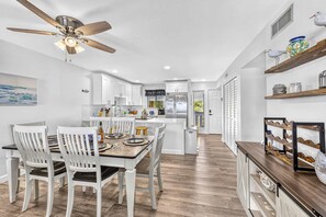 A modern kitchen with white cabinetry, a dining area with a wooden table and white chairs, and a ceiling fan. - Bayfront • Rehabbed • Pickleball • Private Beach (Bradenton Beach)