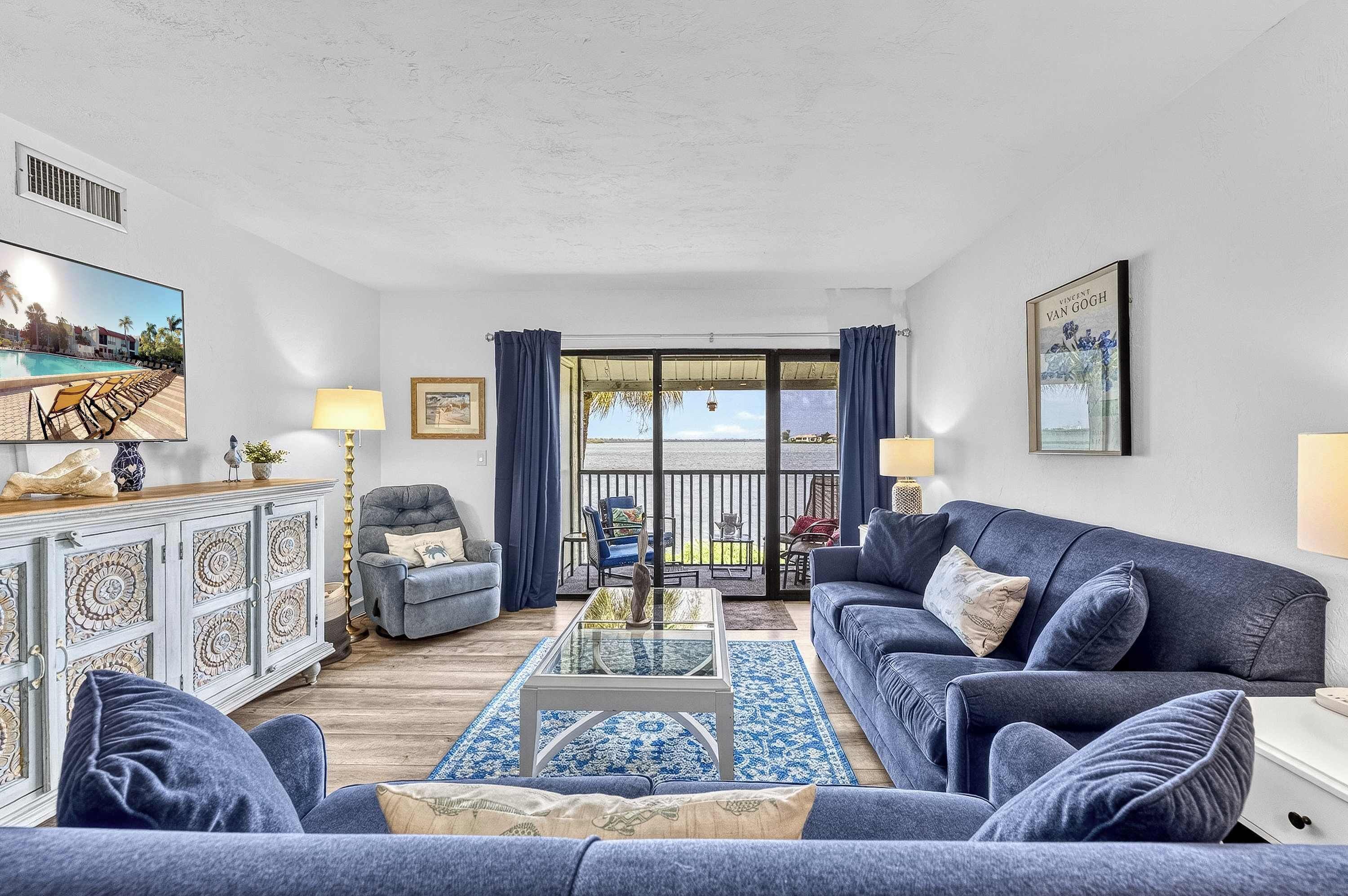 A living room with a sofa, armchairs, a coffee table, and a view of a pool and building through a glass door.