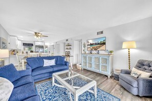 Ein modernes Wohnzimmer mit einem blauen Sofa, einem Glastisch und einem grauen Sessel.