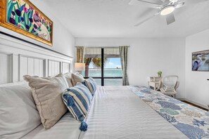 A bedroom with a bed, a desk, a chair, a ceiling fan, and a window with a view of the sea. - Bayfront • Rehabbed • Pickleball • Private Beach (Bradenton Beach)