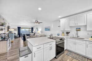 A modern kitchen with white cabinetry, a central island, and a dining area with a view. - Bayfront • Rehabbed • Pickleball • Private Beach (Bradenton Beach)