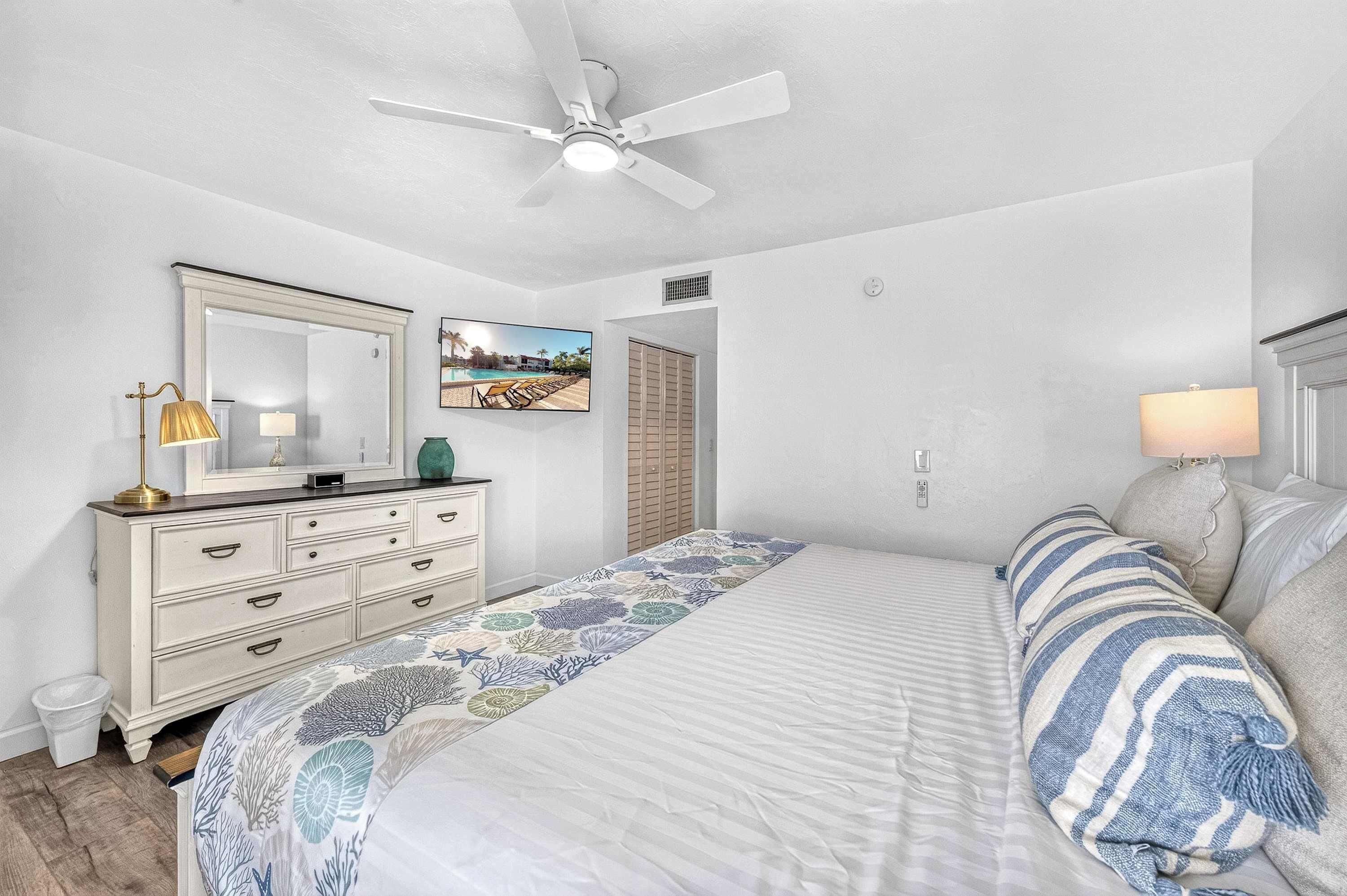 A bedroom with a bed, dresser, mirror, ceiling fan, and a painting on the wall.
