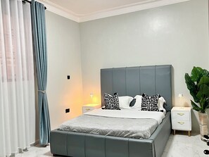 Een slaapkamer met een bed, twee nachtkastjes, een plant in pot en een raam met gordijnen.