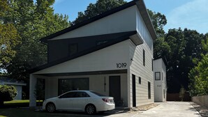 Una moderna casa a due piani con garage, un'auto bianca parcheggiata all'interno e cielo sereno.