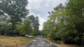Una strada asfaltata con disegni a gesso, circondata da alberi e un'auto bianca parcheggiata sul lato.