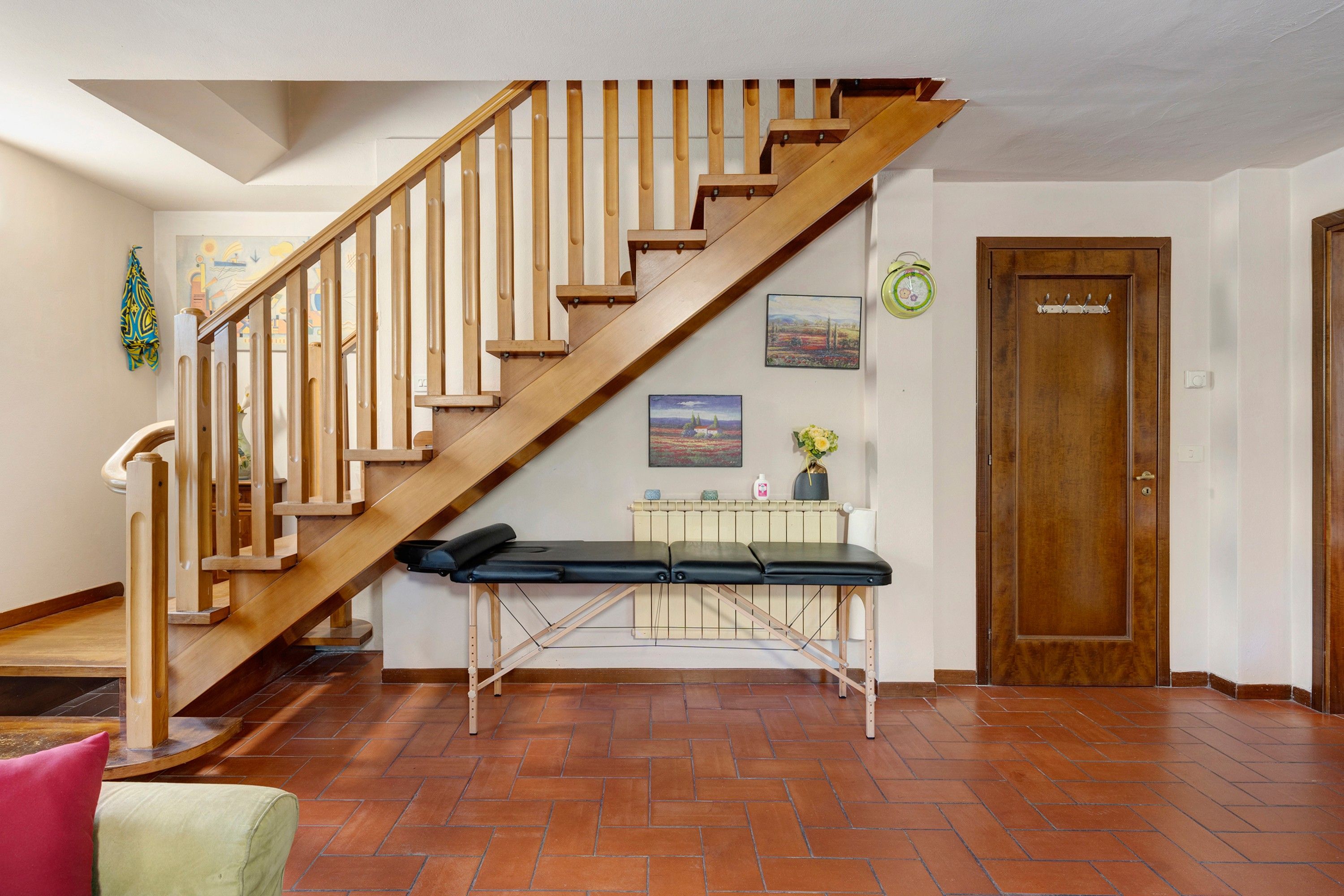A wooden staircase with a handrail, a bench at the bottom, a radiator, and a door with a coat hook.