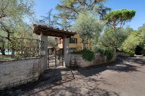 Una entrada protegida con un muro de piedra, una reja metálica y una estructura de pérgola.