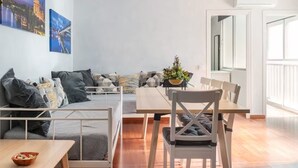 Un salon moderne comprenant un canapé, une table à manger et des chaises, une grande fenêtre et des œuvres d’art accrochées au mur.