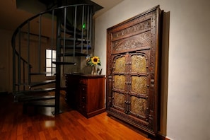 Eine Wendeltreppe, eine Holztür mit aufwendigen Schnitzereien und ein Holzschrank mit einer Vase voller Sonnenblumen.