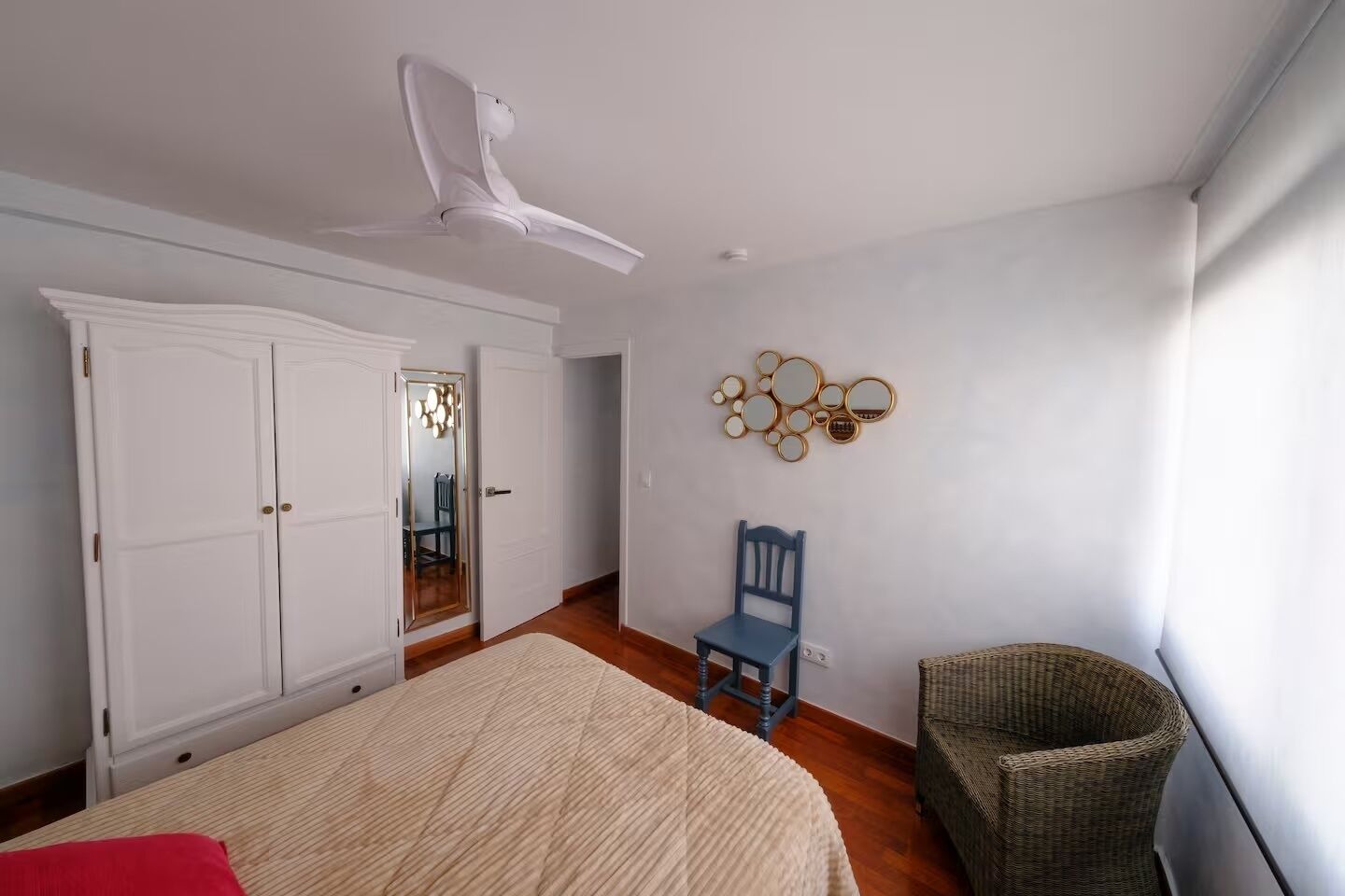 A bedroom with a bed, a chair, a wardrobe, a ceiling fan, and a wall decoration.