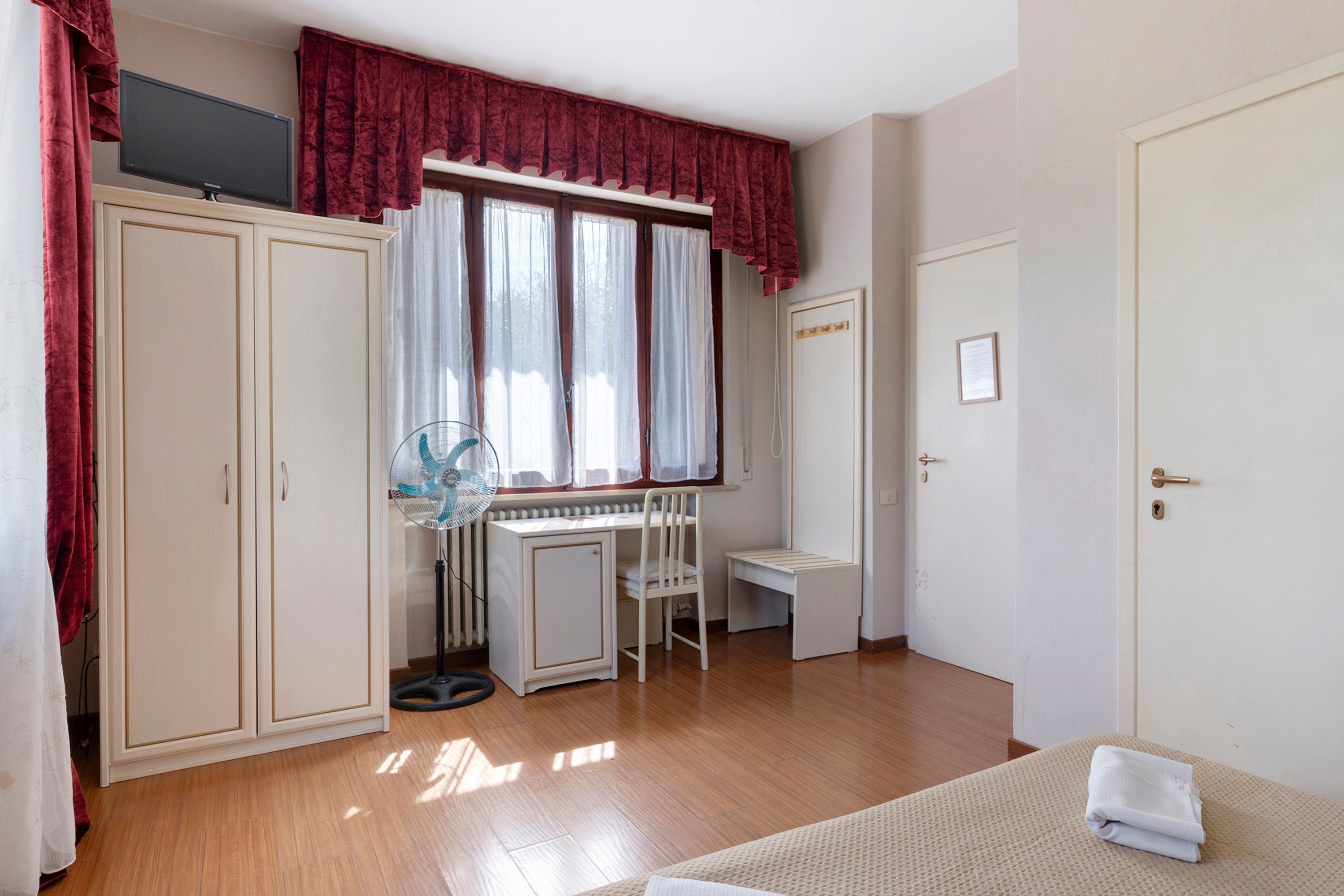 Una stanza con un letto, una scrivania, un termosifone e una finestra con tende.