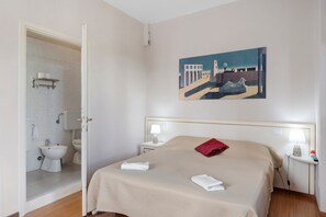 Ein Hotelzimmer mit Bett, einem Gemälde, einem Badezimmer und einem Nachttisch.