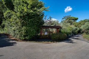 A paved path leading to a small brick structure with a sign, surrounded by dense greenery and trees.