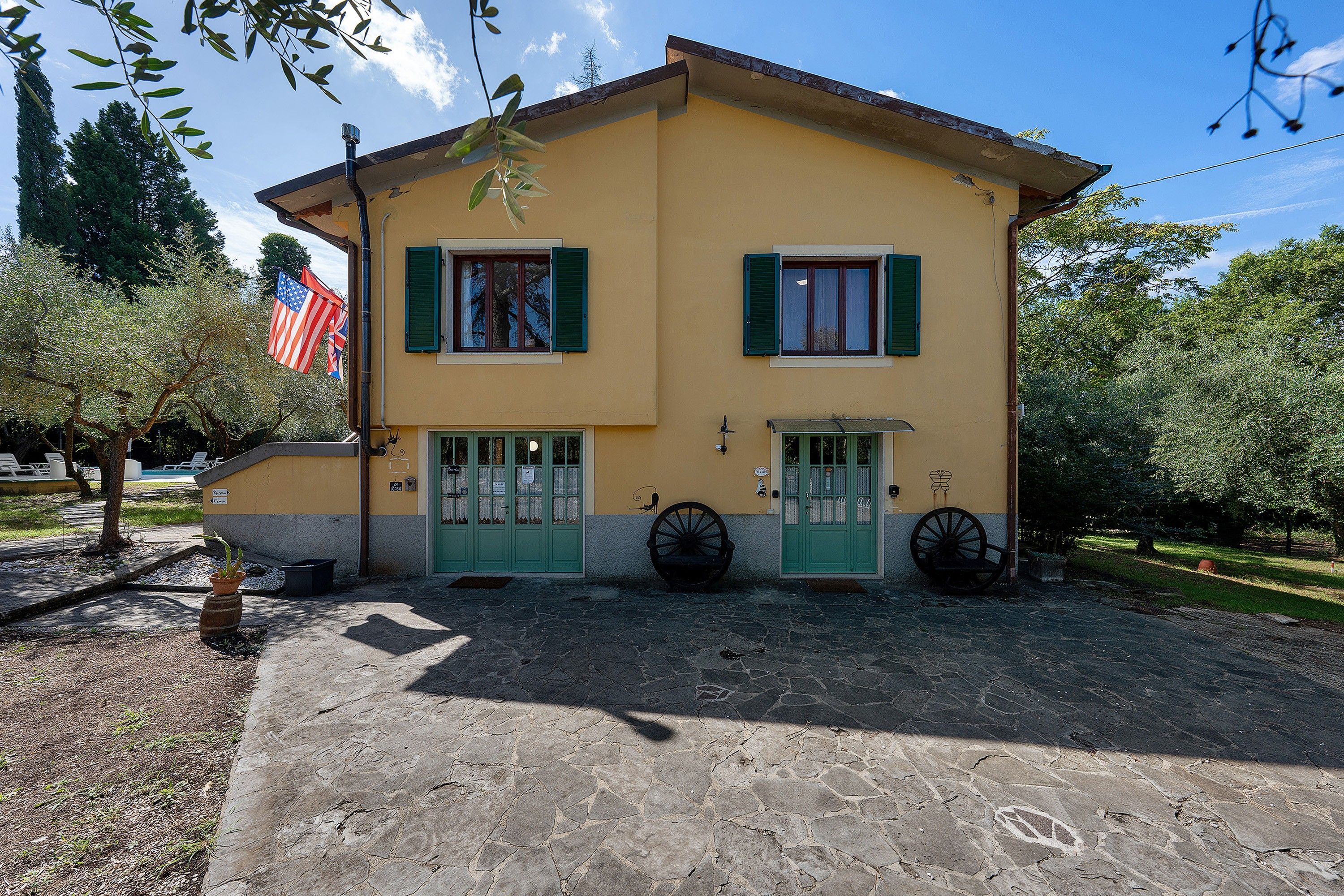 A two-story building with a yellow facade, green shutters, and a stone-paved entrance.