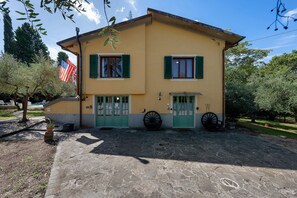 A two-story building with a yellow facade, green shutters, and a stone-paved entrance.