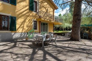 A yellow building with a balcony, outdoor seating, and a tree.