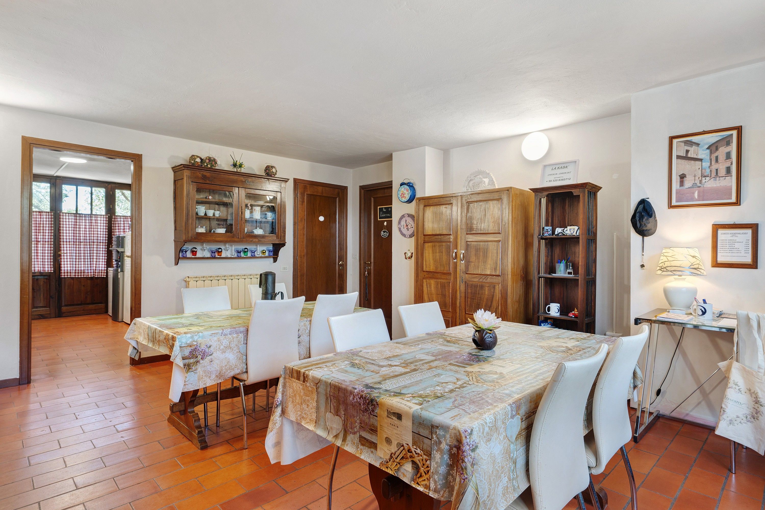 A dining area with a table set for four, surrounded by white chairs. There is a wooden cabinet with glass doors containing kitchenware.