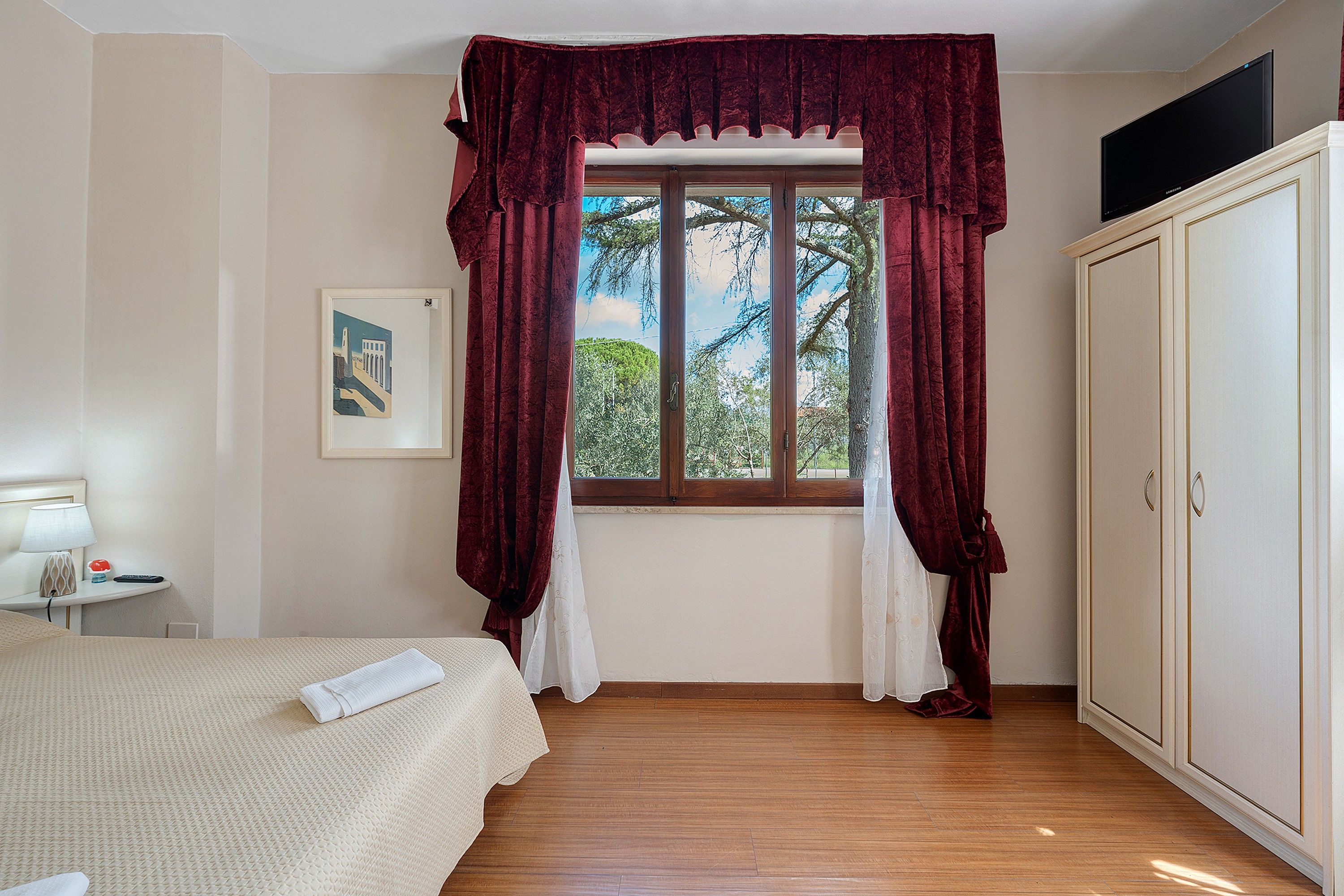 Habitación de hotel con cama, ventana con cortinas, armario y un cuadro en la pared.